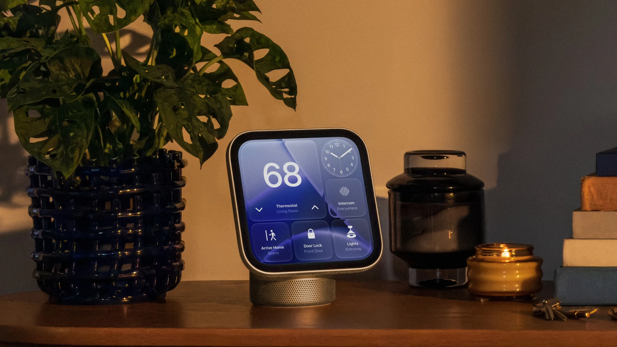 Apple HomeView smart home display on a wooden sideboard next to a plant, a glass vase and a candle, showing thermostat, door lock and light controls